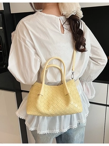 Sac seau tressé jaune pâle porté en bandoulière par un mannequin dans un décor moderne