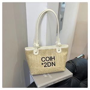 Detail of woven straw tote bag with white leather handles and COIH 2DN embroidery