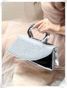 Detail of silver sequin handbag with unique chrome curved handle worn with tulle dress