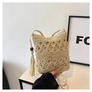 Detail of hand-woven beige bucket bag featuring floral cutouts and tassel with wooden beads