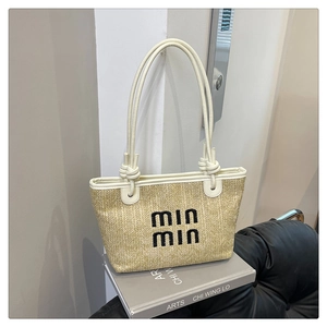 Detail of straw tote bag with black embroidery and cream leather straps on arts book