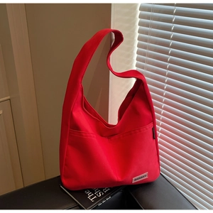 Detail of red canvas shoulder bag with dual front pockets and woven brand label