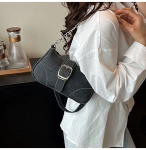 Detailed shot of black denim baguette bag with white stitching and silver square buckle