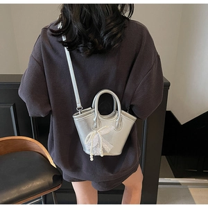 Silver mini bucket bag with lace bow and pearl charms worn by a model in a minimal setting