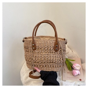 Detail of beige straw bucket bag with brown leather handles and adjustable shoulder strap
