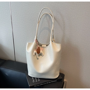 Detail view of cream woven leather tote bag with wing horse charm on a black sofa