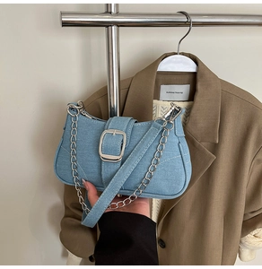 Detail of blue denim baguette bag with silver buckle, metal chain, and white stitching
