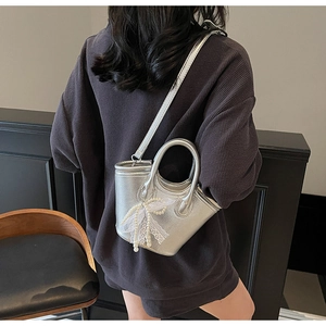 Silver metallic crossbody bucket bag with pearl lace bow charm worn by a model