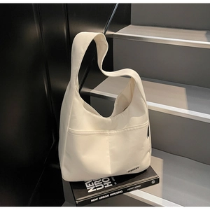 Close-up of minimalist white canvas shoulder bag featuring a front pocket and logo detail