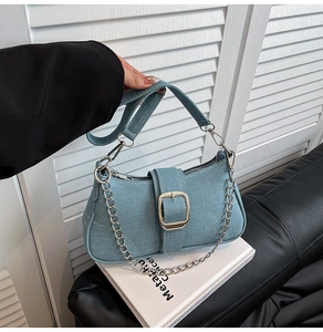 Detail view of denim baguette bag with silver metal buckle and chic chain strap
