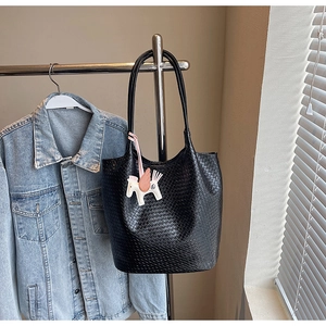 Detail of black woven leather bucket bag with a colorful horse charm on a stand