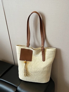 Chic woven straw tote bag with brown leather handles and decorative tassel ornament