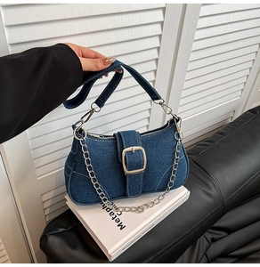 Detail showing the denim fabric texture and silver buckle of the underarm bag