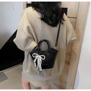 Detail of black glossy bucket bag with white lace and pearl bow charm accessory