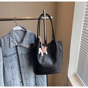 Close-up of black woven tote bag with a small white horse charm on a metal hanger