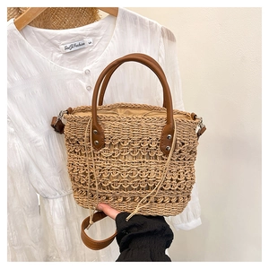 Detail of straw woven tote bag featuring brown faux leather handles and inner drawstring bag