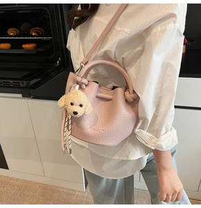 Close-up of pink litchi grain leather bucket bag with a cute puppy plush charm detail