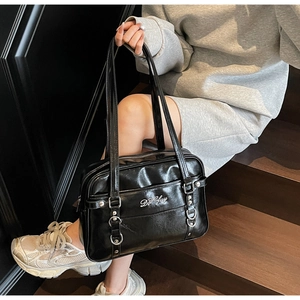 Detail of glossy black patent leather shoulder bag featuring metal logo and buckle accents