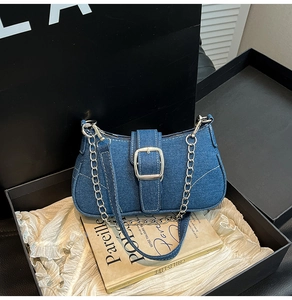 Detail shot of denim crossbody bag with metal buckle and chain inside a luxury gift box