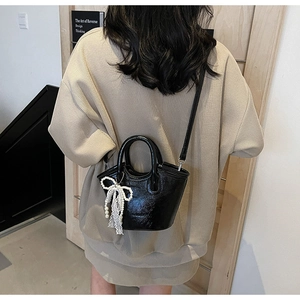 Detail of glossy black patent leather bucket bag with pearl lace bow charm on model