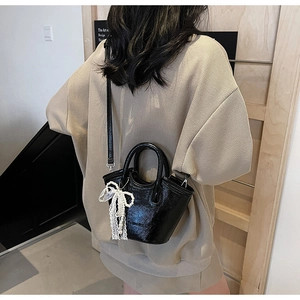 Detail of black glossy textured mini bucket bag with pearl lace bow accessory and long strap