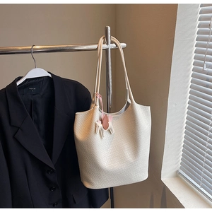 Detail of off-white woven leather tote bag with a small horse charm hanging on the strap