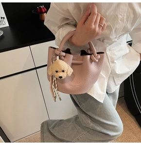 Detail of pink lychee leather bucket bag with cute plush puppy charm and embossed text