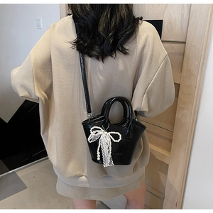 Detail of a black bucket bag with lace bow and pearls, shown in a lifestyle setting