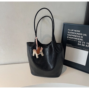Detail of black woven tote bag with slim leather handles and small horse charm