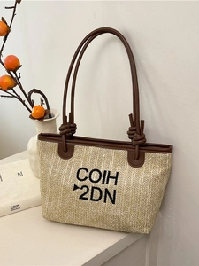 Beige woven straw tote bag with brown leather handles and black embroidered lettering