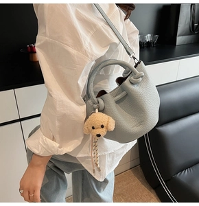Light blue bucket bag with teddy charm shown on shoulder in modern interior setting