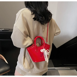 Detail of red patent leather mini bucket bag with pearl and lace bow charm on model
