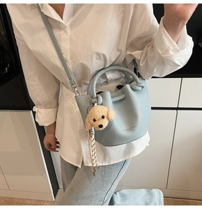 Détail du sac seau bleu clair à motif litchi avec un pendentif ours en peluche marron