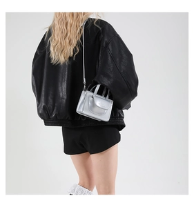 Schicke silberne Mini-Umhängetasche an Model getragen über einer schwarzen Lederjacke