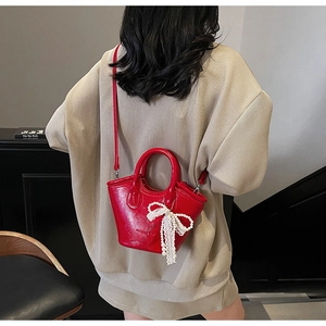 Detail of red patent leather bucket bag with pearl lace bow charm on a model