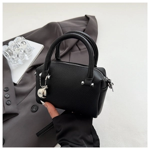 Détail du sac Boston noir en cuir grainé avec ferrures argentées et pendentif porte-bonheur