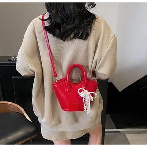 Detail of red glossy leather handbag with pearl lace bow and embossed brand lettering