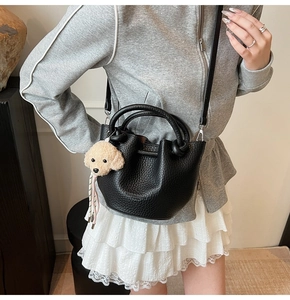 Detail of black lychee grain leather bucket bag with cute plush puppy charm accessory
