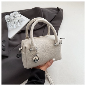 Détail du sac Boston blanc cassé avec pendentif métallique et fermeture éclair argentée