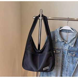 Detail of black tote bag with white contrast stitching and minimalist brand logo