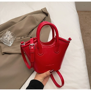 Detail of red glossy leather bucket bag showing top handles and embossed logo texture