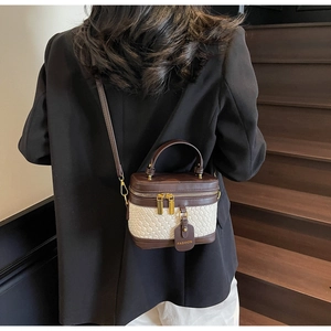 Detail of a mini box bag with brown leather trim and beige woven texture on a model