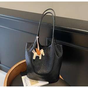 Detail of black woven leather tote bag featuring a decorative pony charm and artistic props