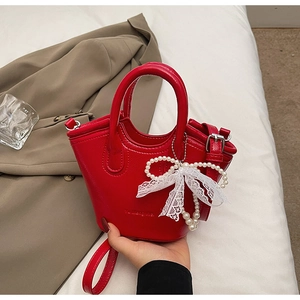 Detail of red bucket bag with litchi texture, pearl charms and white lace bow