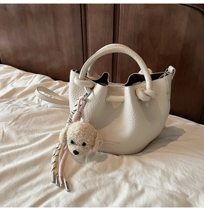 Close-up of white lychee leather bucket bag with cute plush poodle charm and woven strap