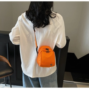 Rear view of model wearing a bright orange nylon crossbody shell bag with black straps
