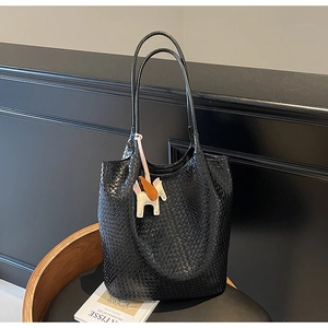 Macro detail of black woven leather tote bag featuring a decorative pegasus charm