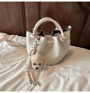 Detail of off-white lychee grain leather bucket bag with a cute puppy plush charm