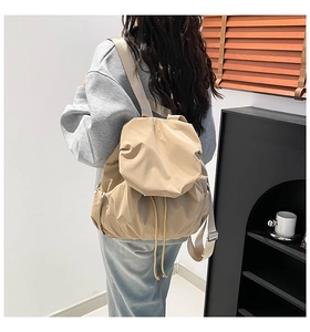 Close-up of beige nylon drawstring backpack with flap and side pocket on a model