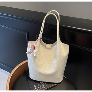 Detail of cream tote bag featuring crocodile embossed texture and a horse charm